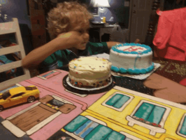 a little boy is sitting at a table with two birthday cakes on it