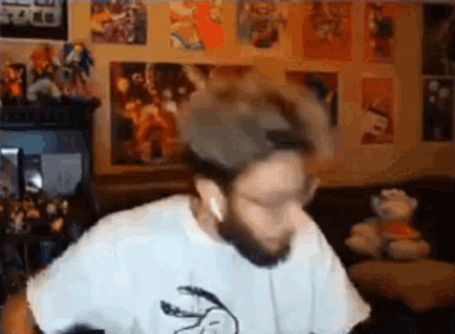 a man with a beard is sitting in a living room wearing headphones and a white shirt .