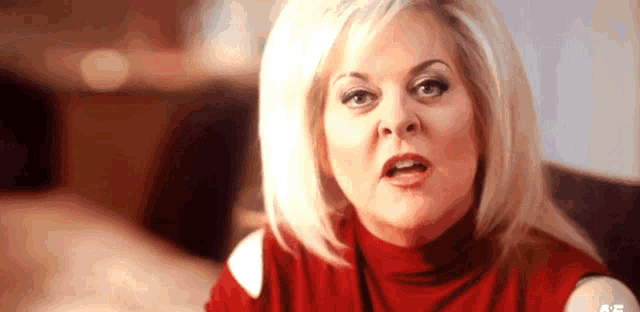 a woman in a red turtleneck is making a funny face while sitting on a couch .