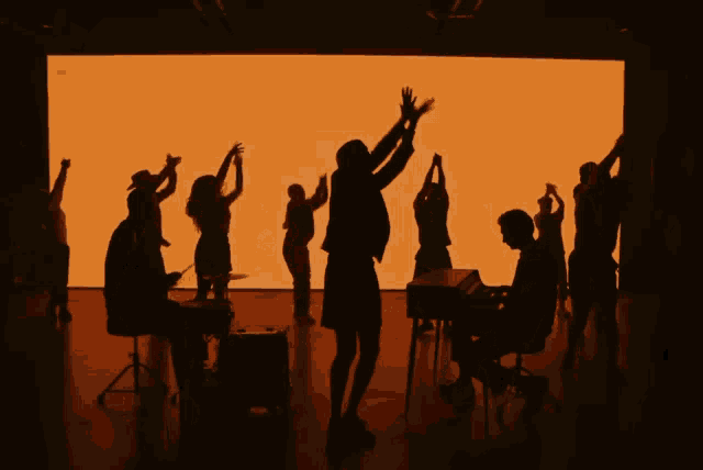 a group of people are dancing in front of an orange screen