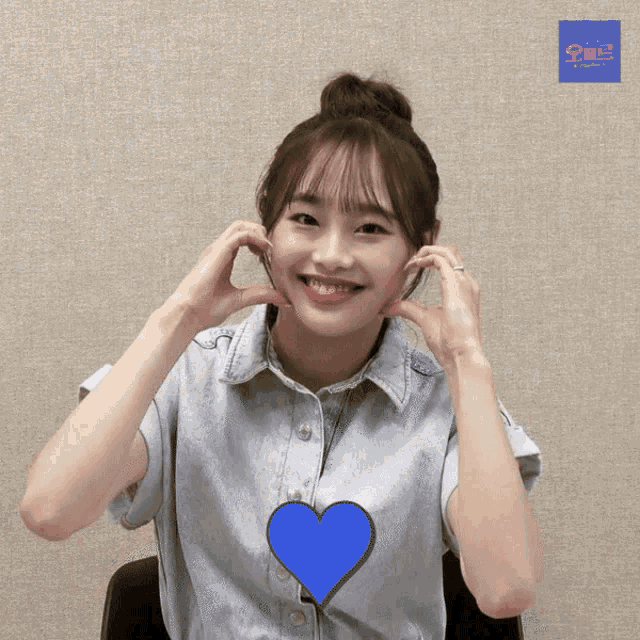 a woman making a heart shape with her hands in front of a sign that says ' 우리 ' on it