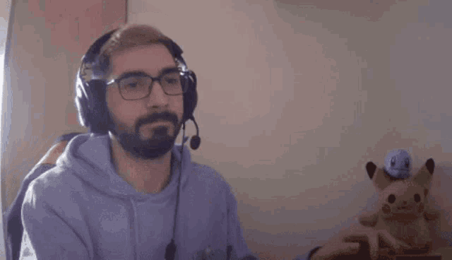 a man wearing headphones and glasses is sitting at a desk next to a stuffed animal .