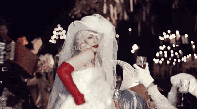 a bride in a white dress and red gloves holds a glass of wine
