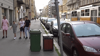 a group of people walking down a street with a red car parked on the sidewalk