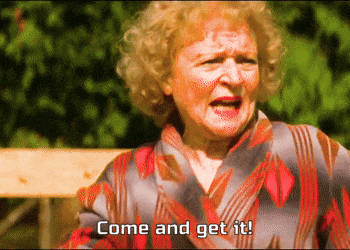 an elderly woman says come and get it in front of a wooden bench