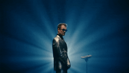 a man in a suit and sunglasses is standing in front of a blue background