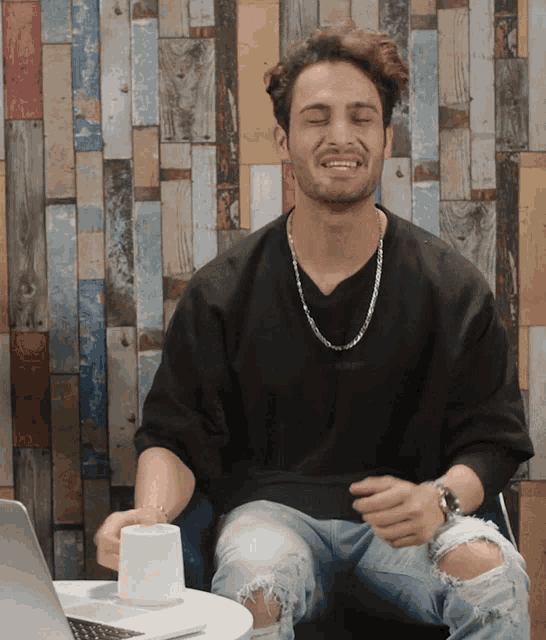 a man wearing ripped jeans is sitting in front of a wooden wall