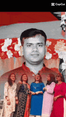 a group of women are posing in front of a man 's portrait .