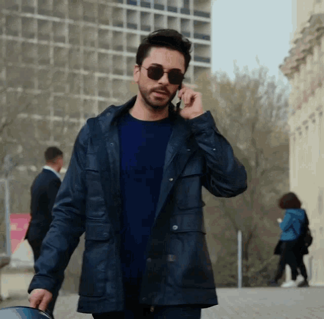 a man wearing sunglasses and a blue jacket is talking on his cell phone