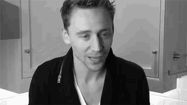 a black and white photo of a man wearing a black sweater and a white shirt .
