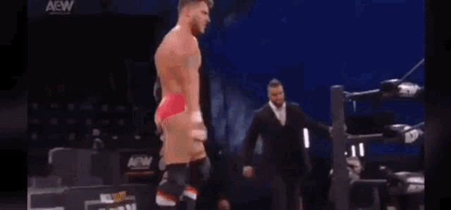 a man in red shorts is standing on a stage in a wrestling ring with a man in a suit behind him .