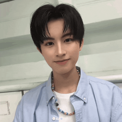 a young man wearing a blue shirt and a necklace