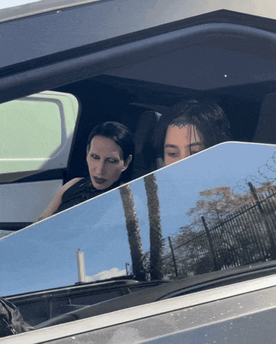 a man and a woman are sitting in a car with a reflection of palm trees in the window