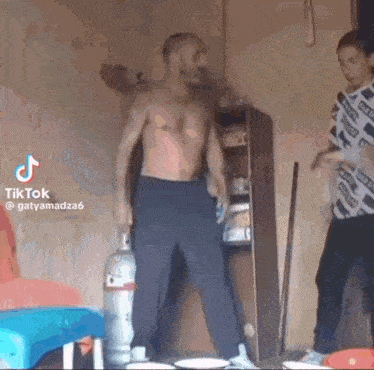 a man without a shirt is standing in a room holding a propane cylinder .