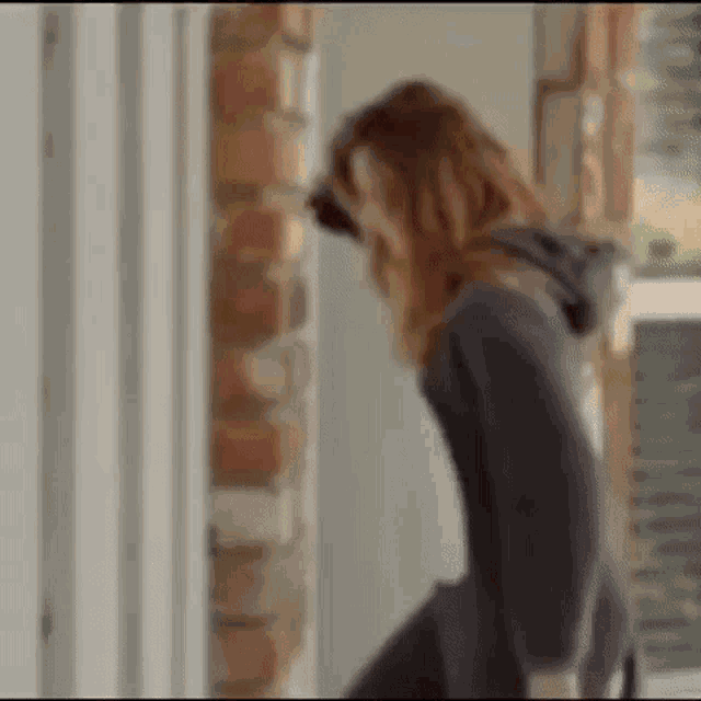 a woman is standing in front of a brick wall looking through a door .