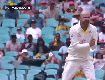 a man in a white cricket uniform is standing in front of a crowd of people in a stadium .