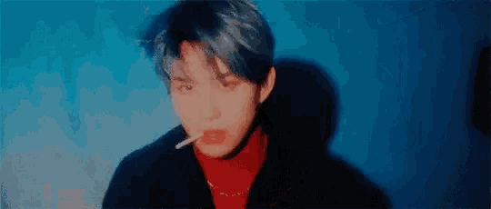 a young man is smoking a cigarette in front of a blue background .