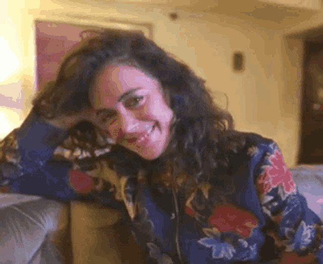 a woman is sitting on a couch with her hand in her hair and smiling .