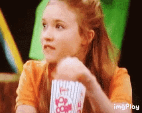 a girl is holding a bucket of popcorn in her hand and eating it .