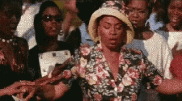 a woman wearing a floral shirt and a hat is standing in a crowd of people .