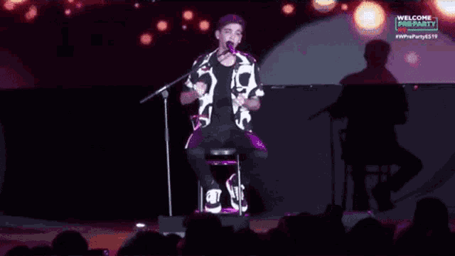 a man singing into a microphone in front of a screen that says welcome to the party