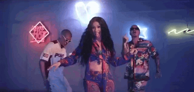 a woman is dancing with two men in a room in front of neon lights .
