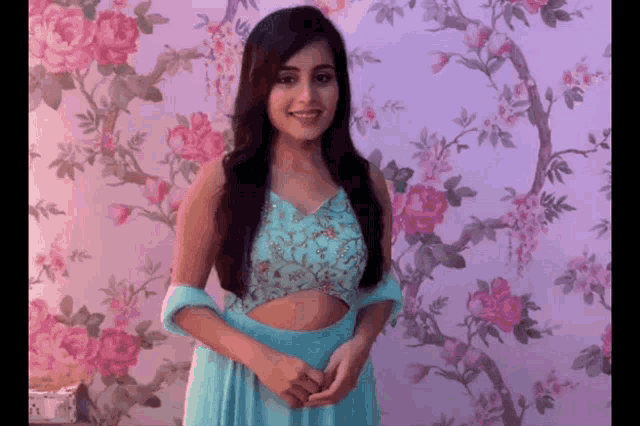a woman in a blue dress is smiling in front of a floral wallpaper