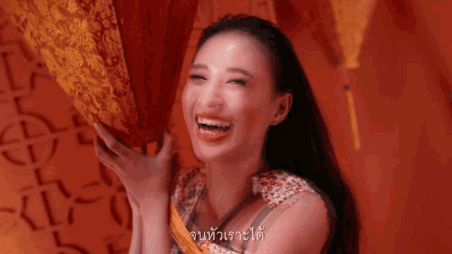 a woman is smiling and holding a fan in front of a wall with chinese writing