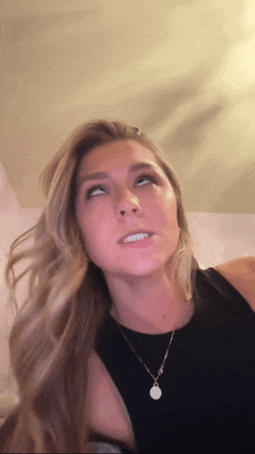 a woman wearing a black top and a necklace looks up