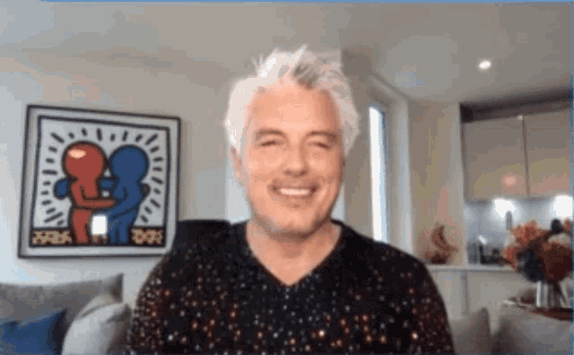 a man is smiling in front of a framed painting of two people hugging