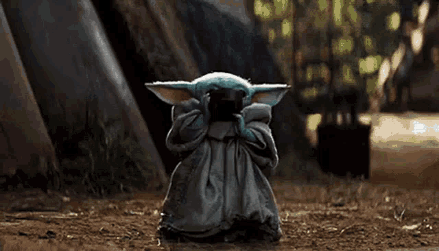 a baby yoda is standing on a dirt road holding a cup of tea .