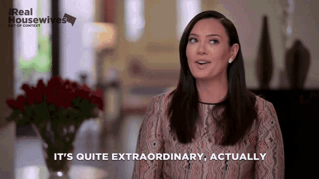 a woman says " it 's quite extraordinary actually " in front of a vase of red roses