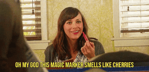 a woman is smiling while holding a marker that smells like cherries .