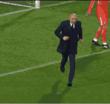 a man in a suit and tie is walking on a soccer field .