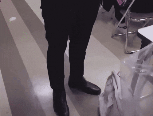 a person wearing black pants and black shoes is standing next to a chair