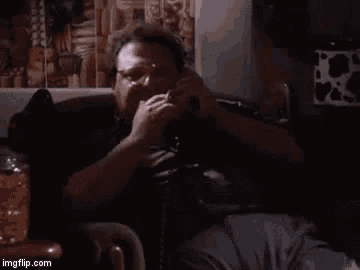 a man is sitting on a couch talking on a cell phone and the words excellent are visible .