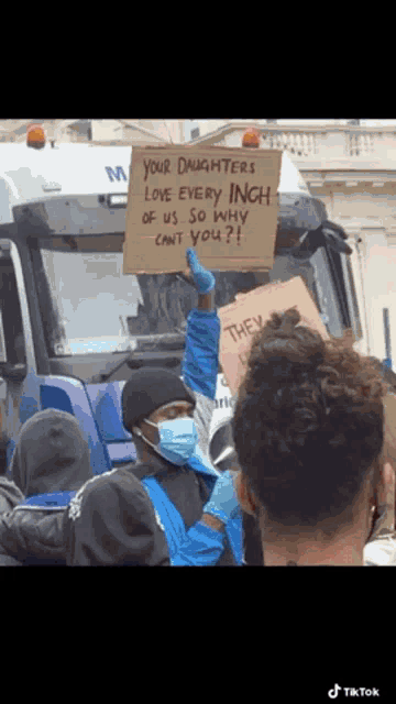 a man wearing a mask holds up a sign that says your daughters love every inch of us so why can 't you