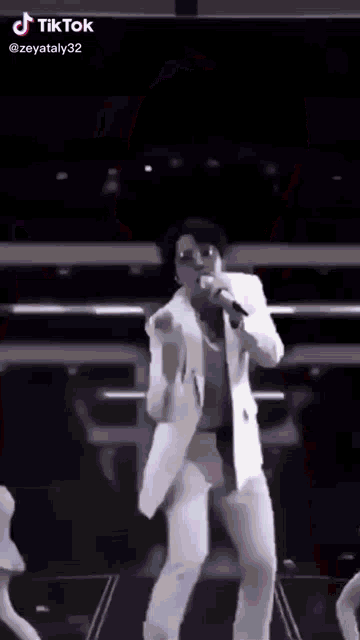 a man in a white suit is singing into a microphone on stage .