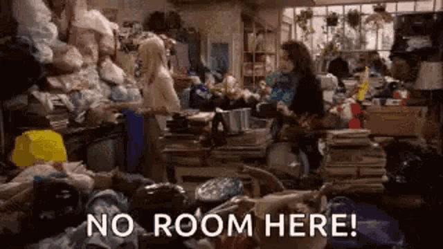 a woman is standing in a room filled with lots of stuff and a sign that says `` no room here '' .