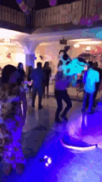 a group of people are dancing in a room with purple lights and balloons .