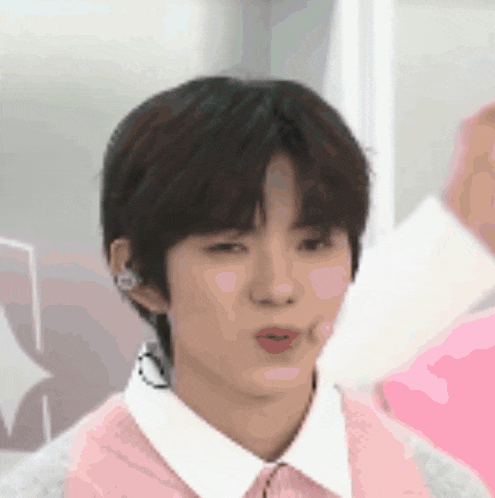 a young man wearing a pink sweater and a white shirt is making a face .