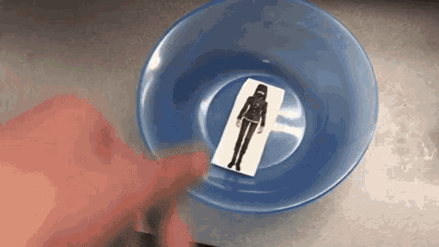 a person is holding a piece of paper with a picture of a girl on it in a bowl of water .