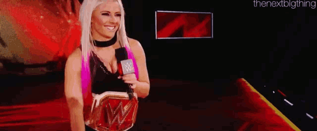 a woman is holding a wrestling championship belt and talking into a microphone on a stage .