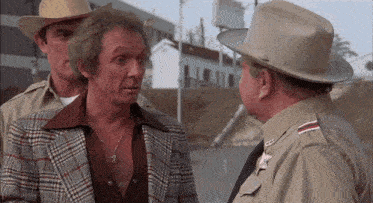 a man in a plaid jacket and cowboy hat talks to a sheriff