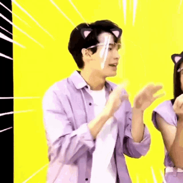 a man in a purple shirt is wearing a cat ear headband and a clear face shield .