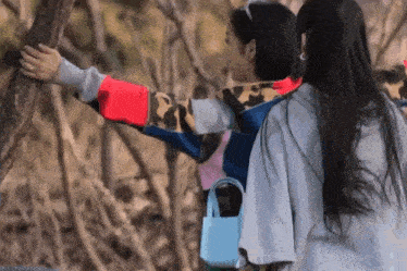 two women are standing next to each other in the woods and one is holding a tree branch .