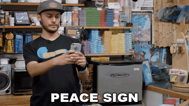 a man holding a cell phone in a store with the words peace sign below him