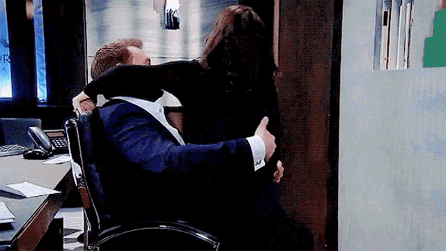 a man in a suit is hugging a woman who is sitting in a chair