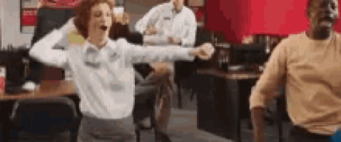 a woman is dancing in an office while a man watches .