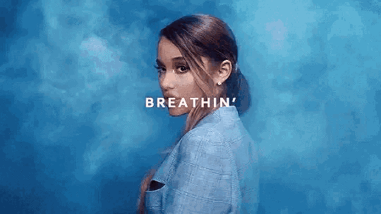 ariana grande is wearing a blue jacket and standing in front of a blue background with smoke coming out of her mouth .